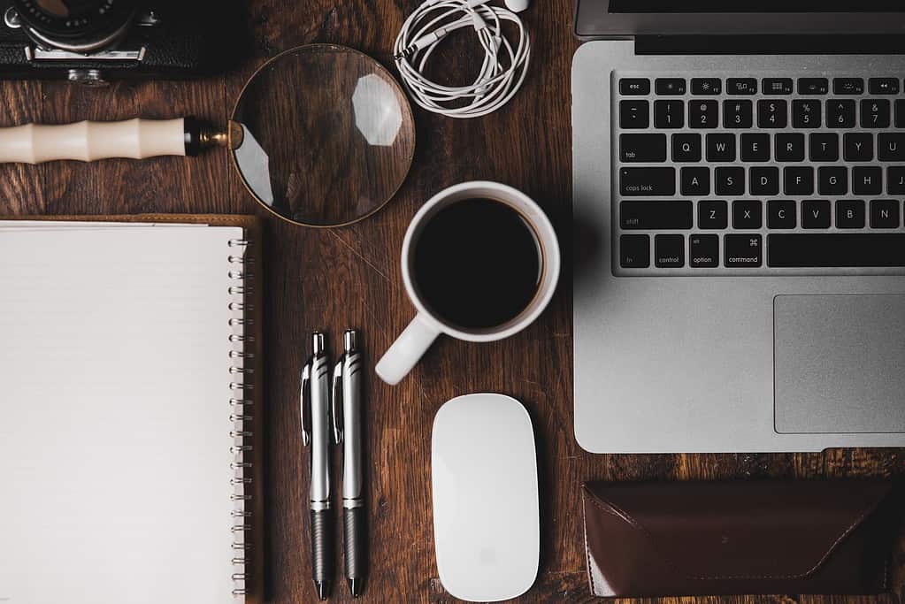 cluttered desk with coffee, computer, and notebook